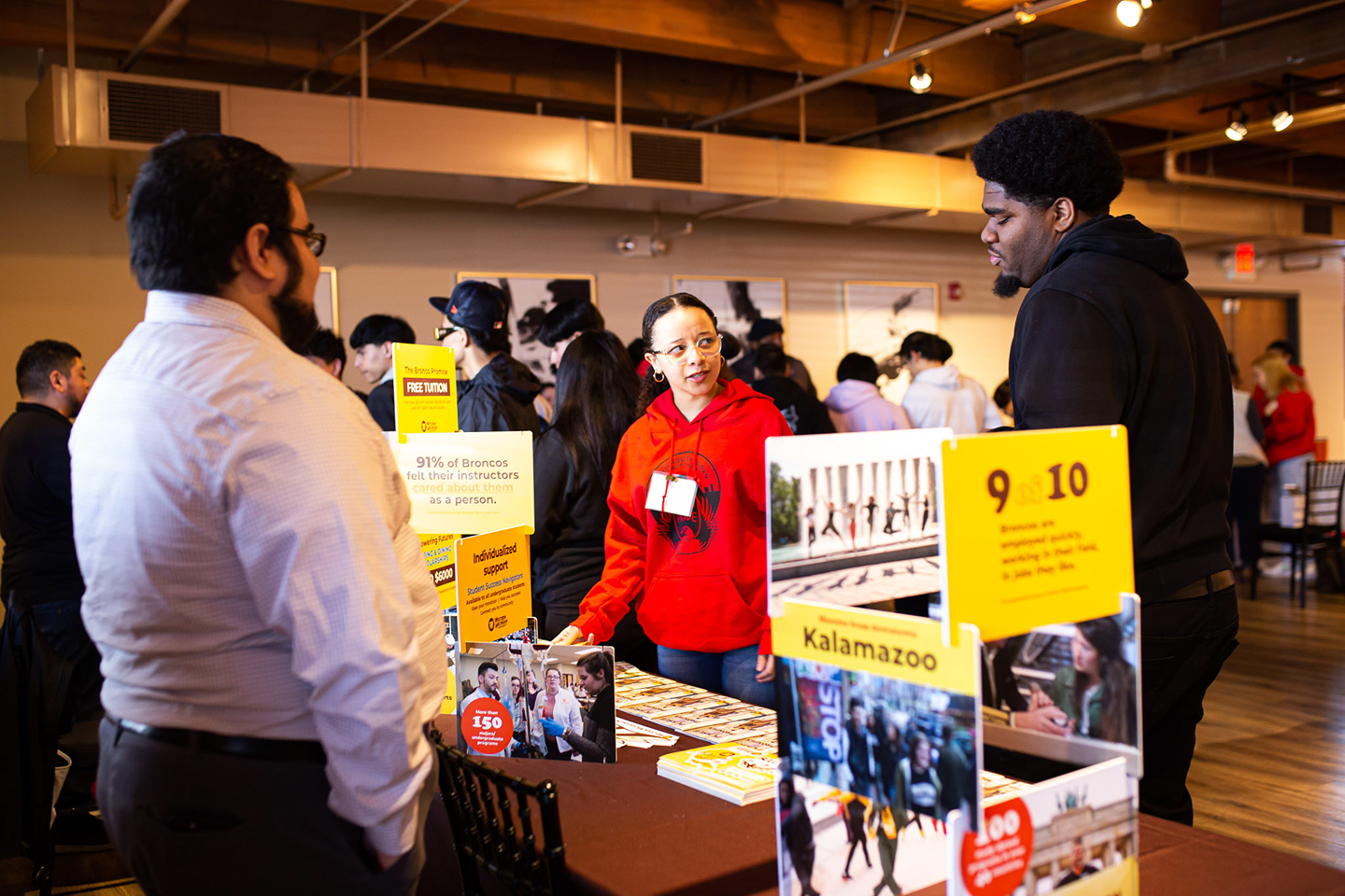 Two students approaching an information table about scholarships at a Challenge Scholars event to support students' access to information and resources about college.
