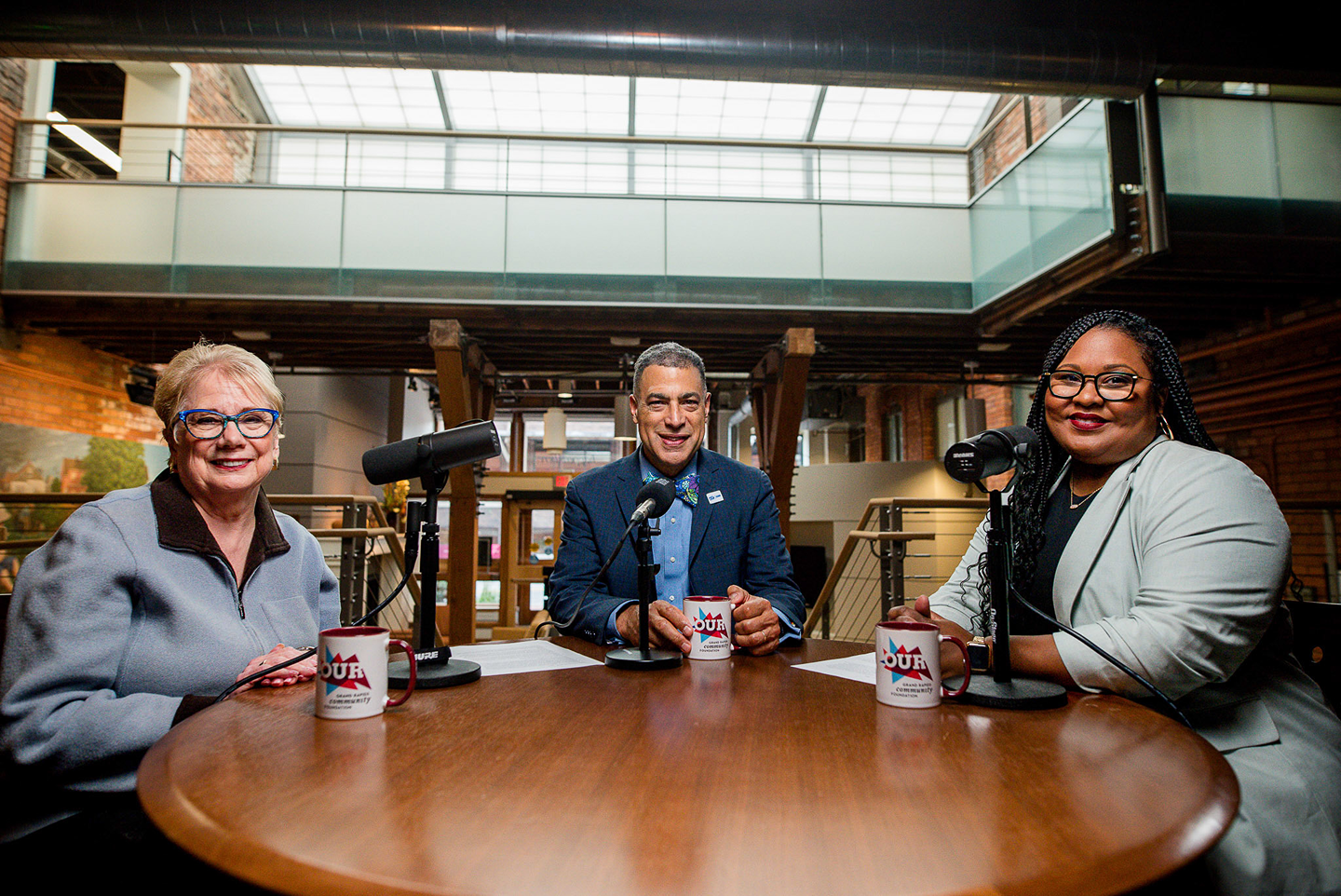Three people sitting at a round table, which is set up with microphones and coffee cups. All are facing the camera and smiling. From left to right: Diana R. Sieger, president, Kyle D. Caldwell, Board of Trustees chair, Ashley Rene Lee, vice president of strategic communications.