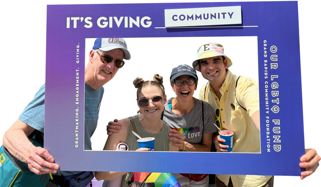 Four people smile and hold frozen treats behind a purple frame that reads “It’s Giving Community” and “Our LGBTQ Fund” at a Grand Rapids Community Foundation event.