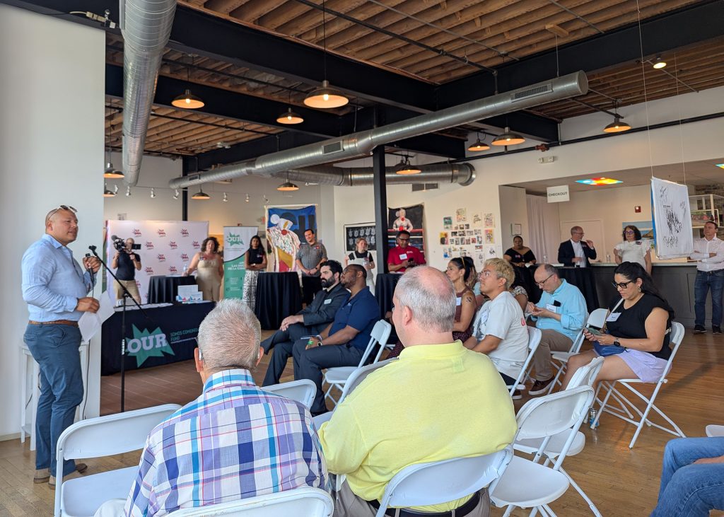 A community meeting inside a modern event space, where a speaker addresses a seated group of residents and partners during a Grand Rapids Community Foundation gathering.